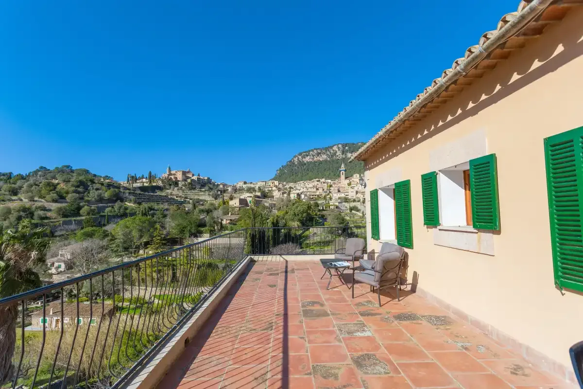A tiled terrace with outdoor seating overlooks a hillside village.