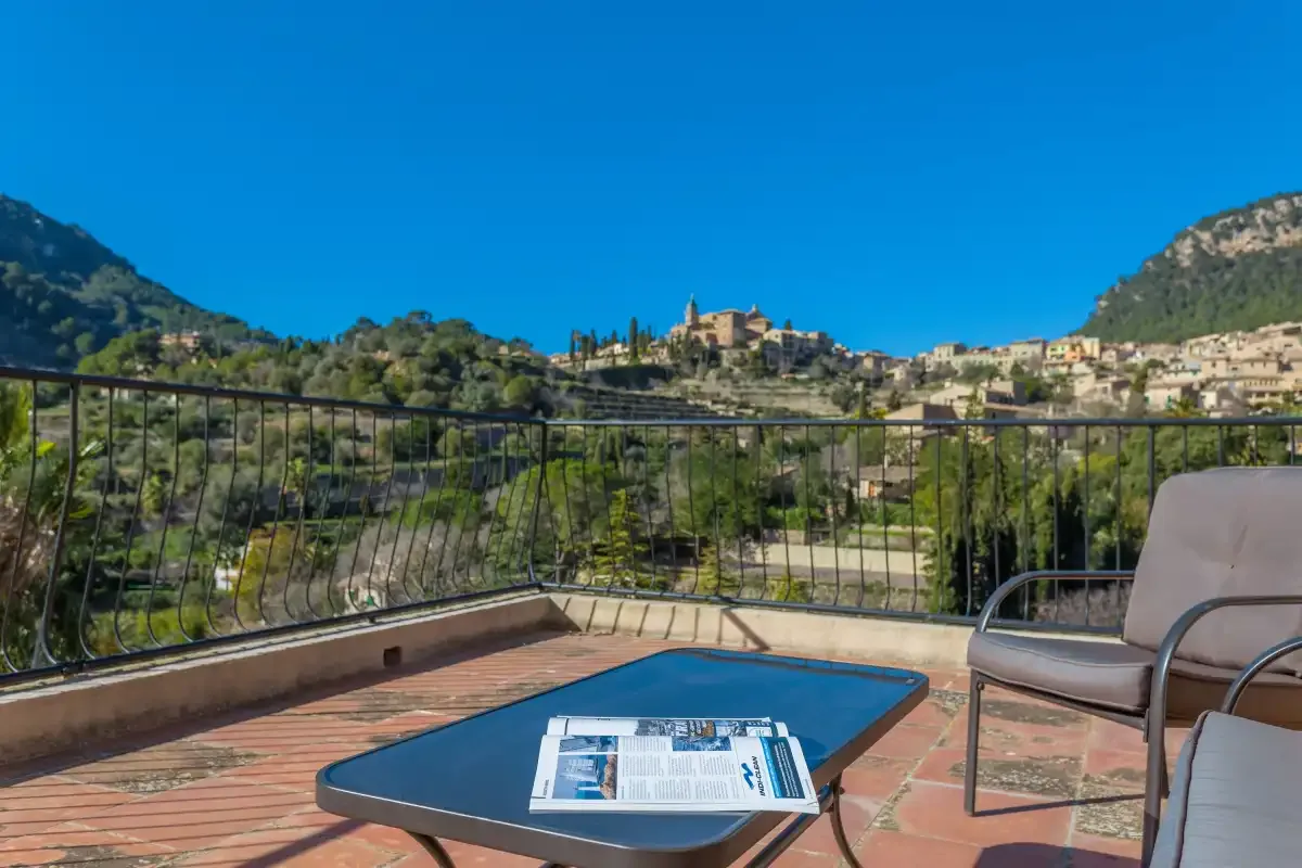 A tiled terrace overlooks a hillside village, with a table and seating in the foreground.