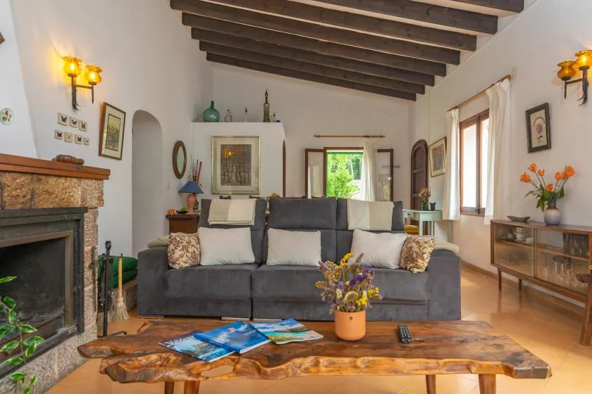 A living room with a gray sofa beneath exposed wooden ceiling beams.