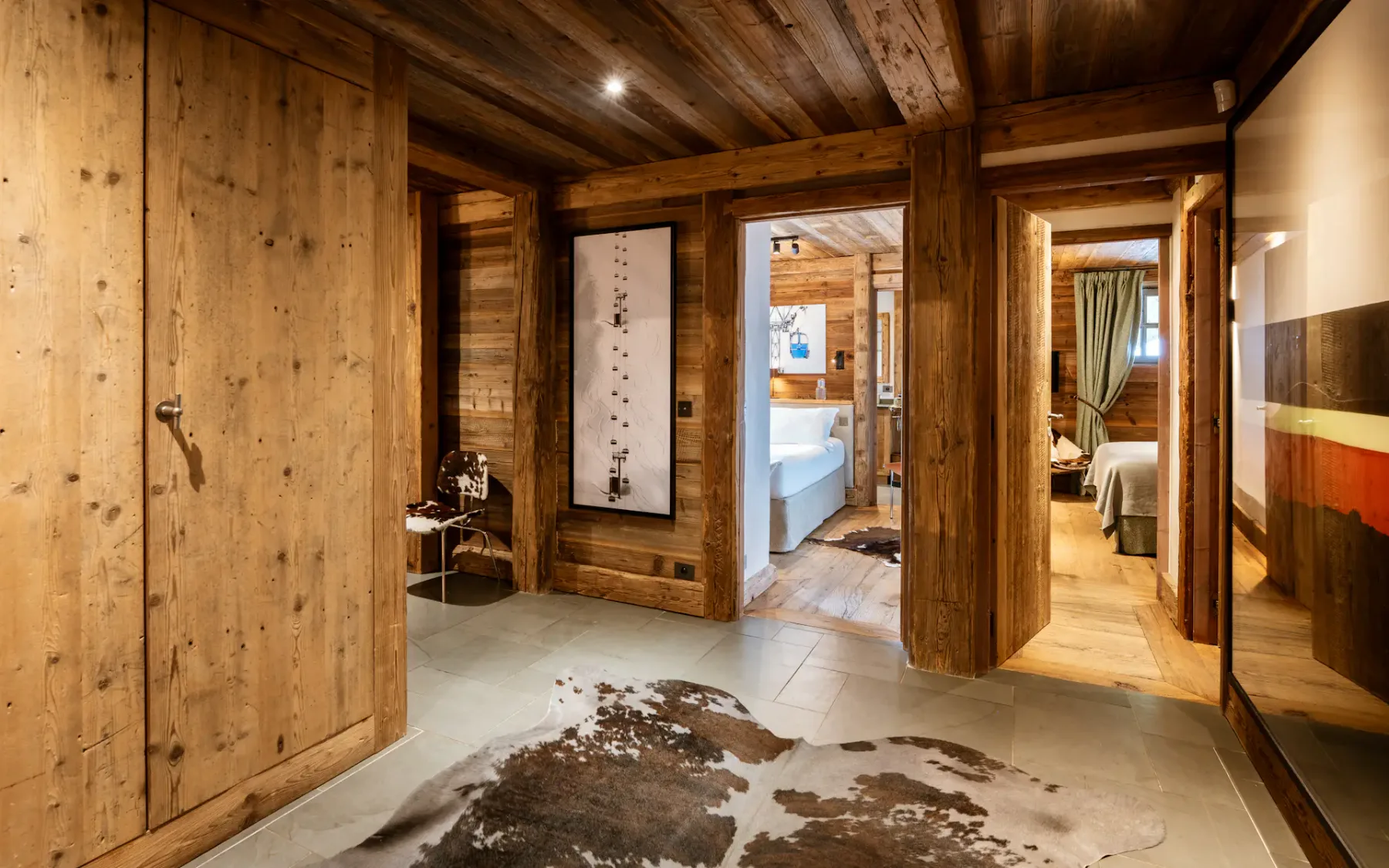 Rustic wooden interior with a cowhide rug, open doorways leading to a bedroom, and a large wardrobe. Warm lighting enhances the cozy ambiance.