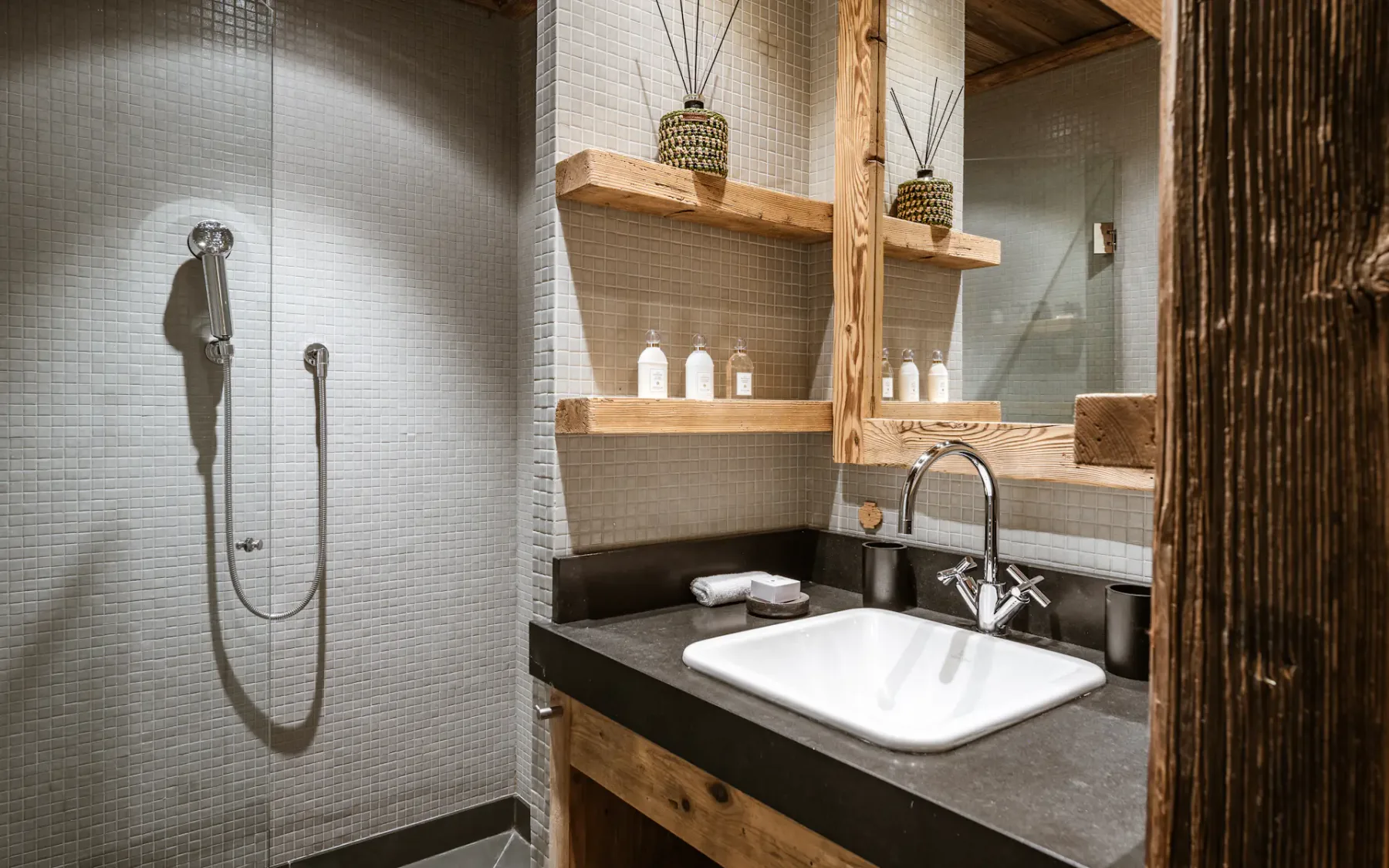 Modern bathroom with a walk-in shower, a rectangular sink on a dark countertop, wooden shelves, and decorative items.