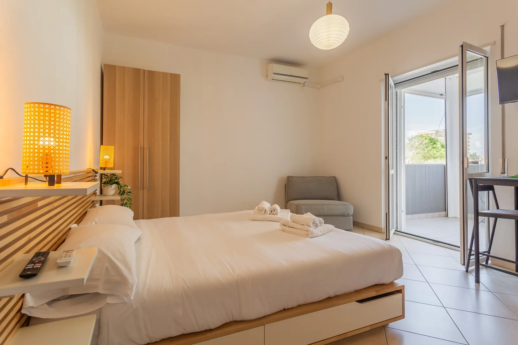 A bright bedroom with a neatly made bed and an open balcony door.