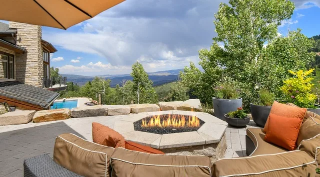 An outdoor patio seating area surrounds a stone fire pit, with mountain views.
