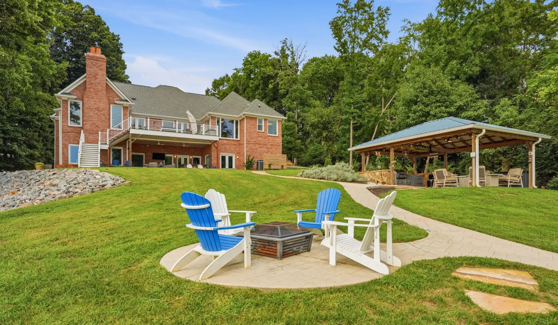 A brick house and covered outdoor seating area overlook a grassy yard.