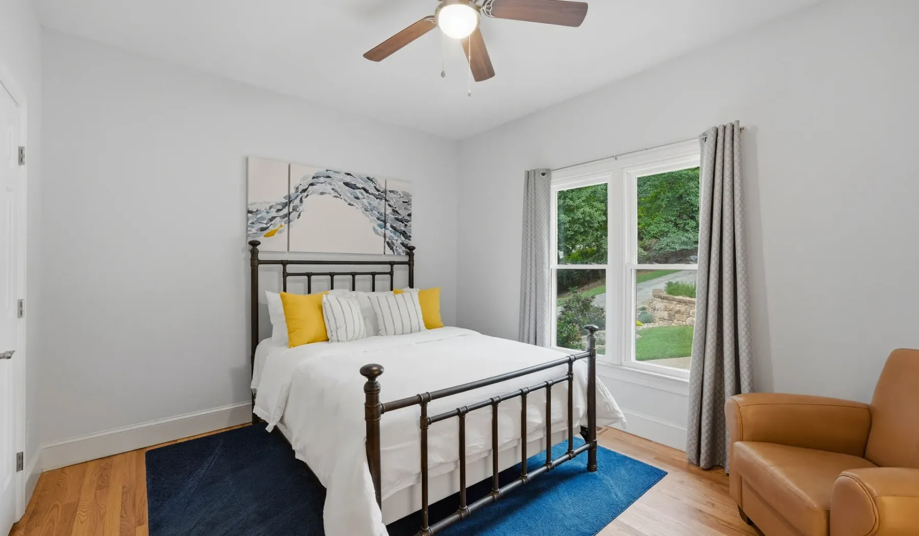 A bright bedroom with a bed, a large window, and a cushioned armchair.