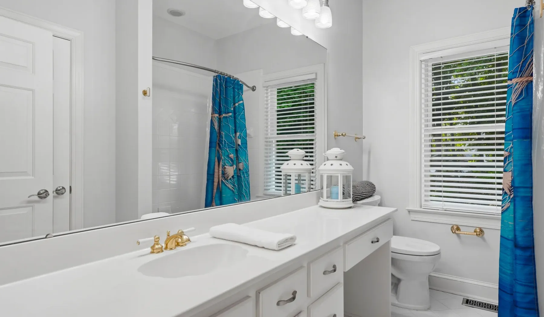 A bright bathroom with a white vanity, mirror, and blue shower curtain.