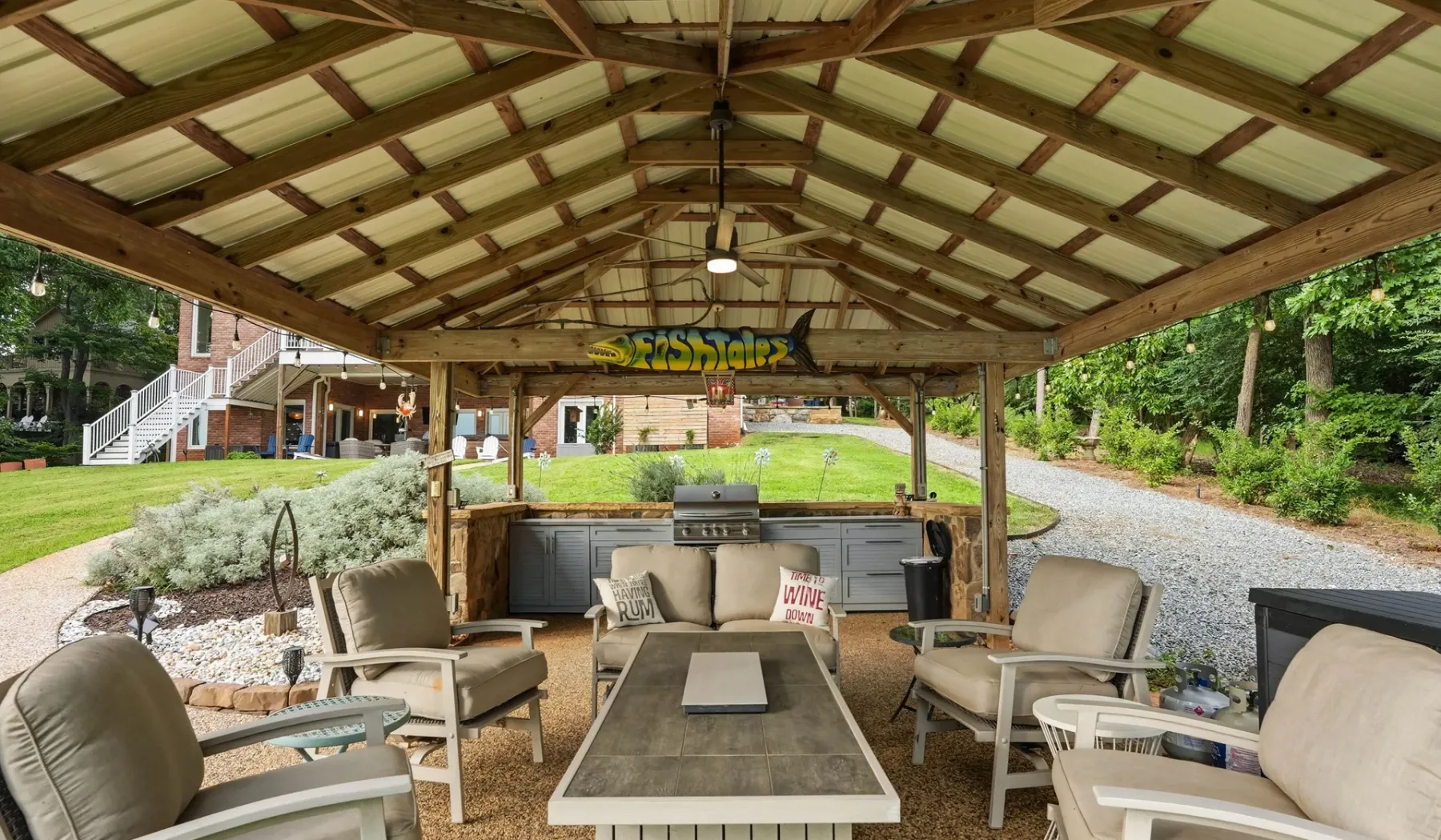 A covered outdoor seating area with a long table and chairs overlooks a green lawn.