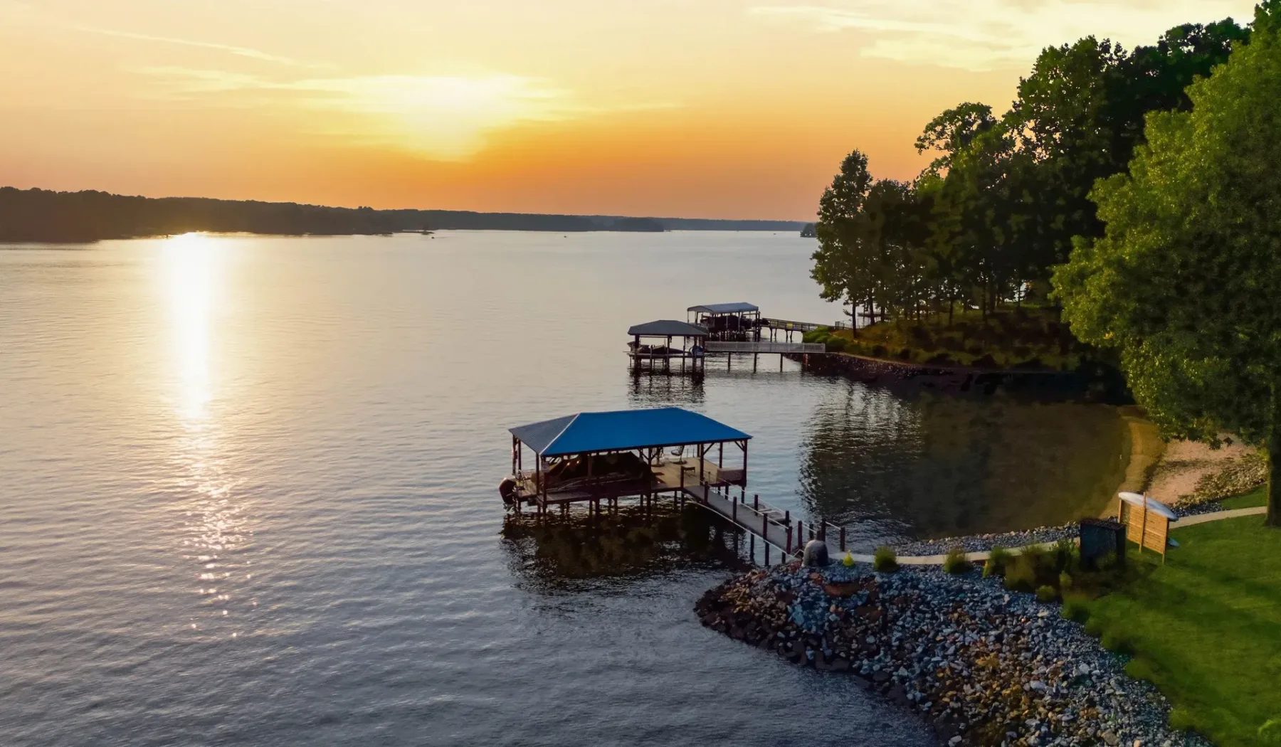 A lakeside scene at sunset with covered docks along the wooded shore.