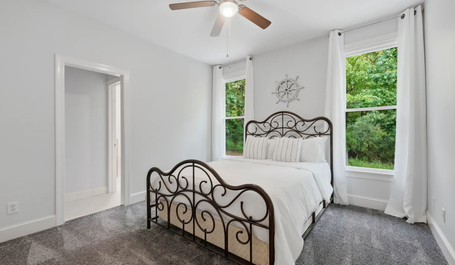 A bright bedroom with a white bed, dark metal frame, and tall windows.
