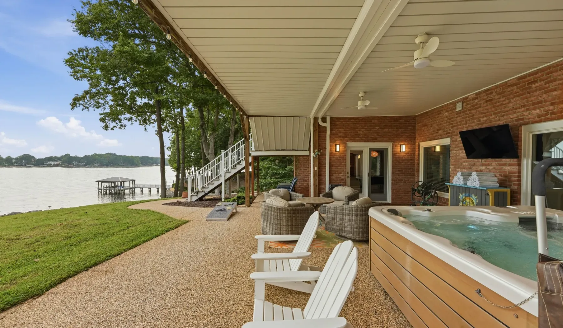 A covered lakeside patio features outdoor seating and a hot tub beside the water.