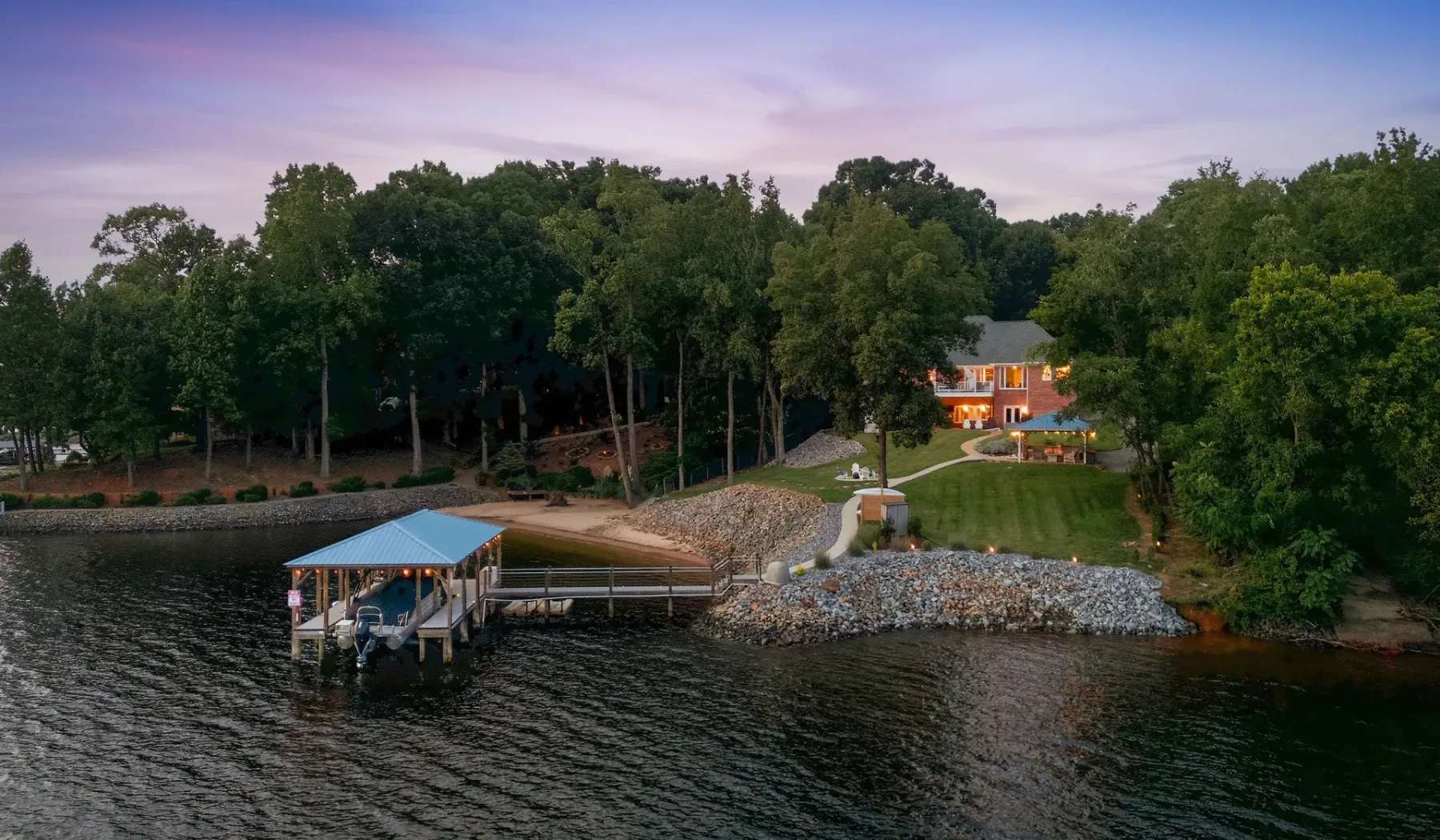 A waterfront house and dock sit beside a tree-lined shore at dusk.