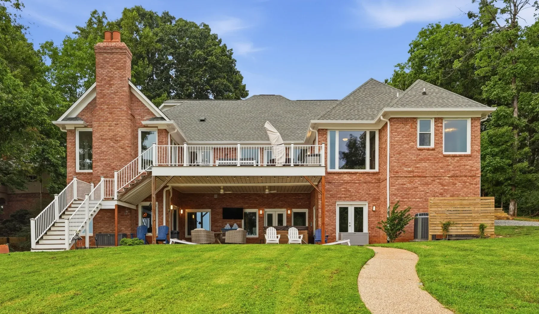 A brick house with a raised deck overlooks a broad green lawn.