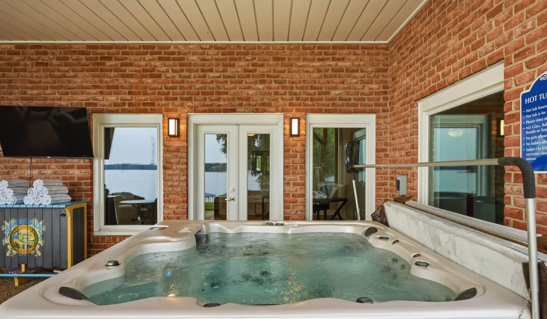 An indoor hot tub sits in a brick-walled room with windows and glass doors.