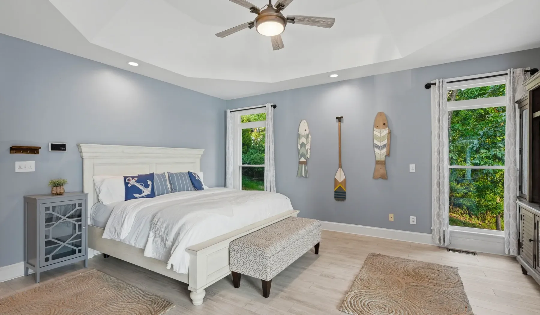 A bright bedroom with a white bed, gray walls, and windows overlooking greenery.