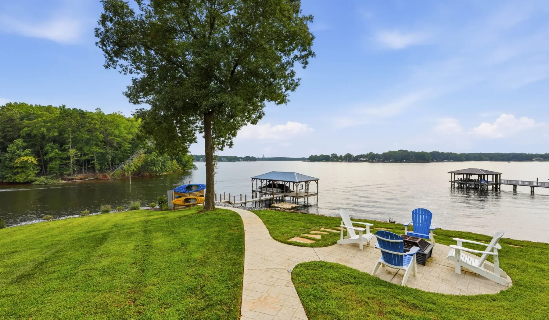 A grassy lakeside yard with a paved path, outdoor seating, and a dock.