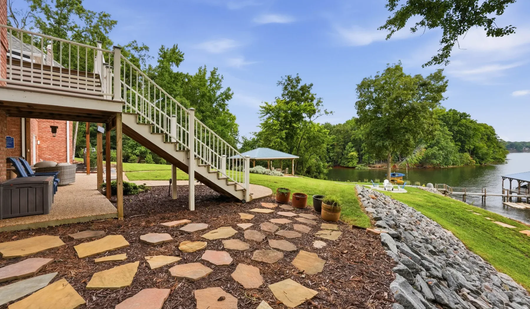 A landscaped lakeside yard has stone stepping paths and a deck staircase.