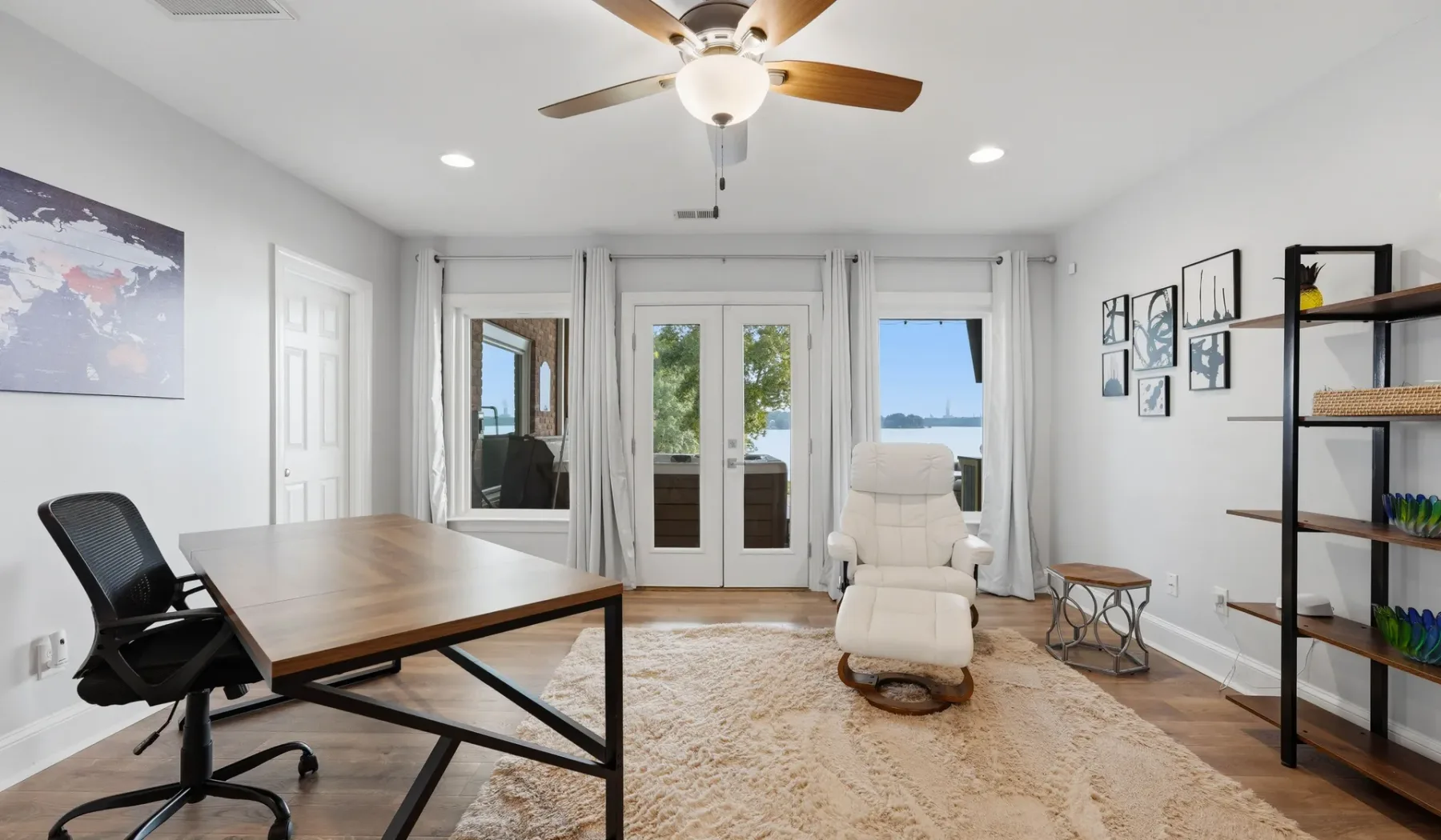 A bright room has a wooden desk, a reclining seat, and glass doors opening to a balcony.