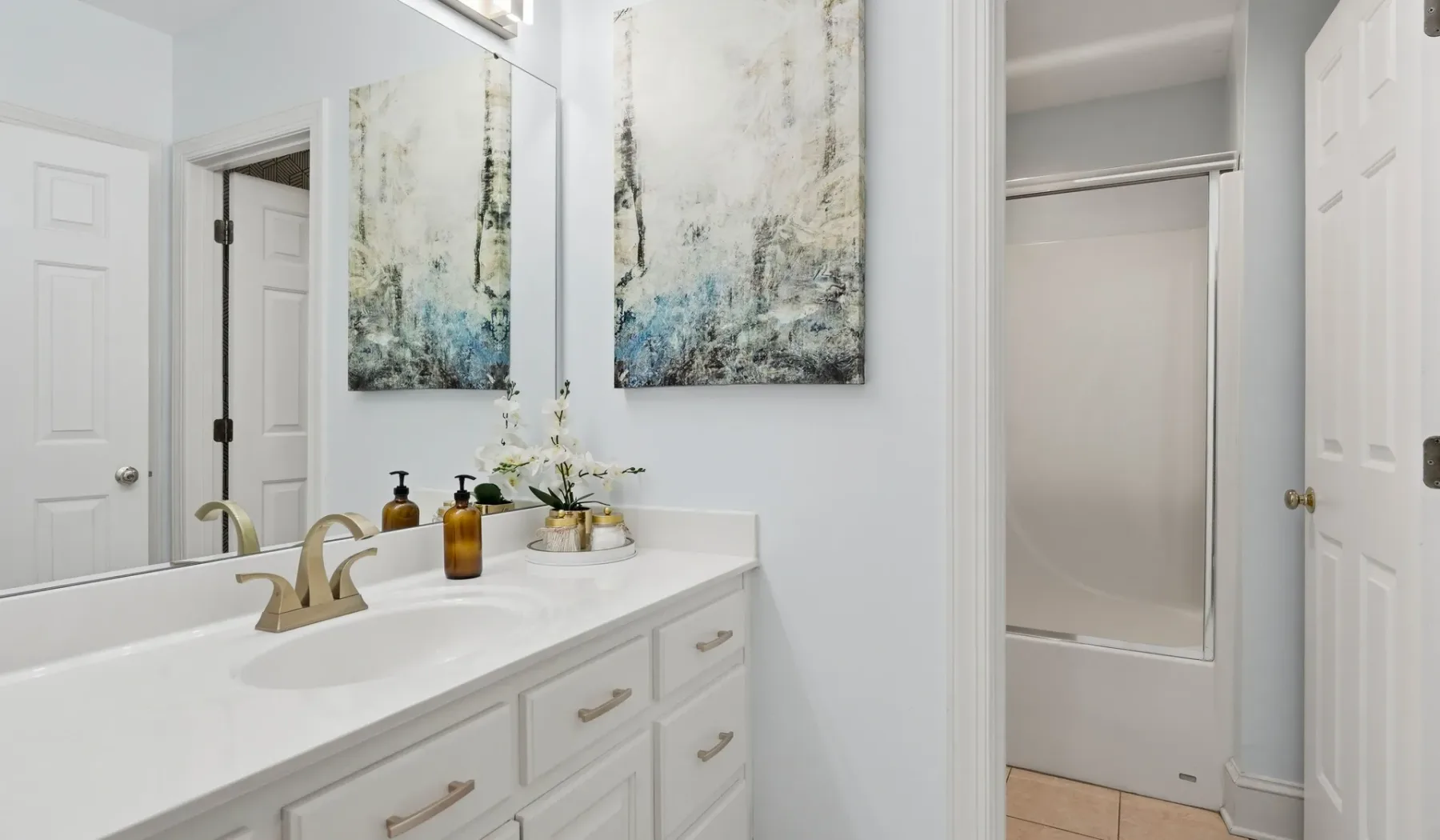 A bright bathroom with a long vanity, wall art, and a shower.