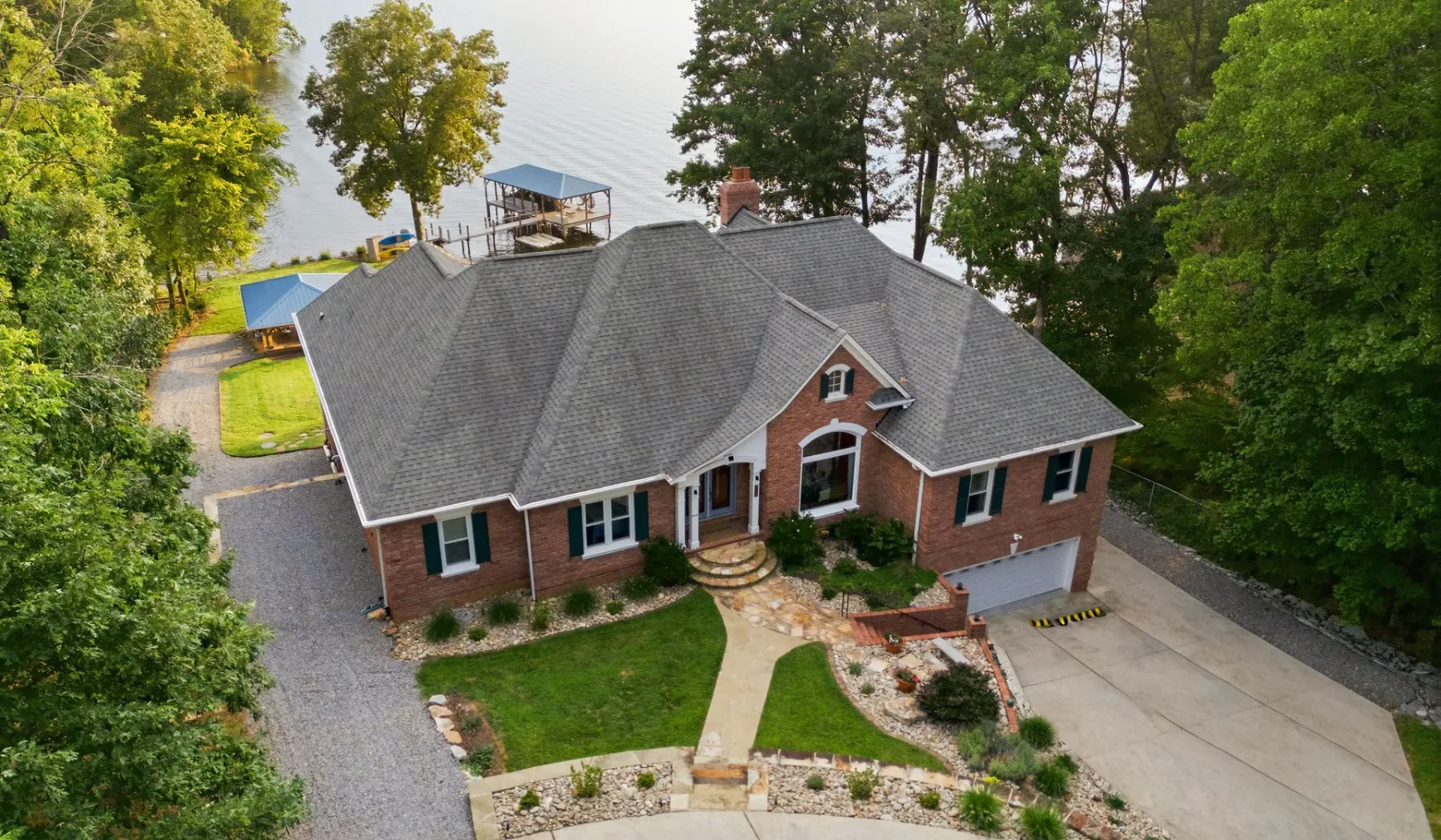 Aerial view of a brick house beside a tree-lined waterfront.