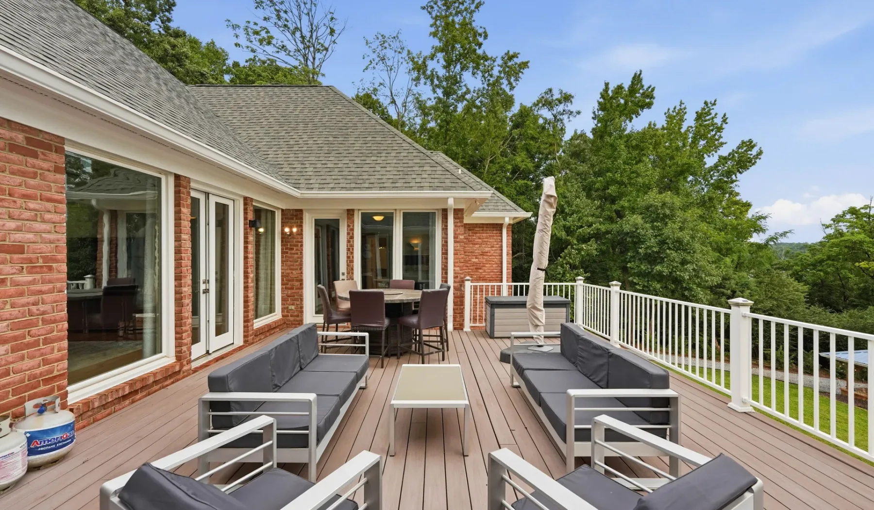 An outdoor deck with seating and a dining table overlooks a tree-lined landscape.
