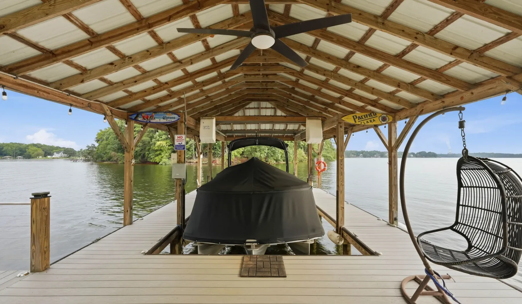 A covered lakeside dock shelters a boat, with a hanging chair nearby.