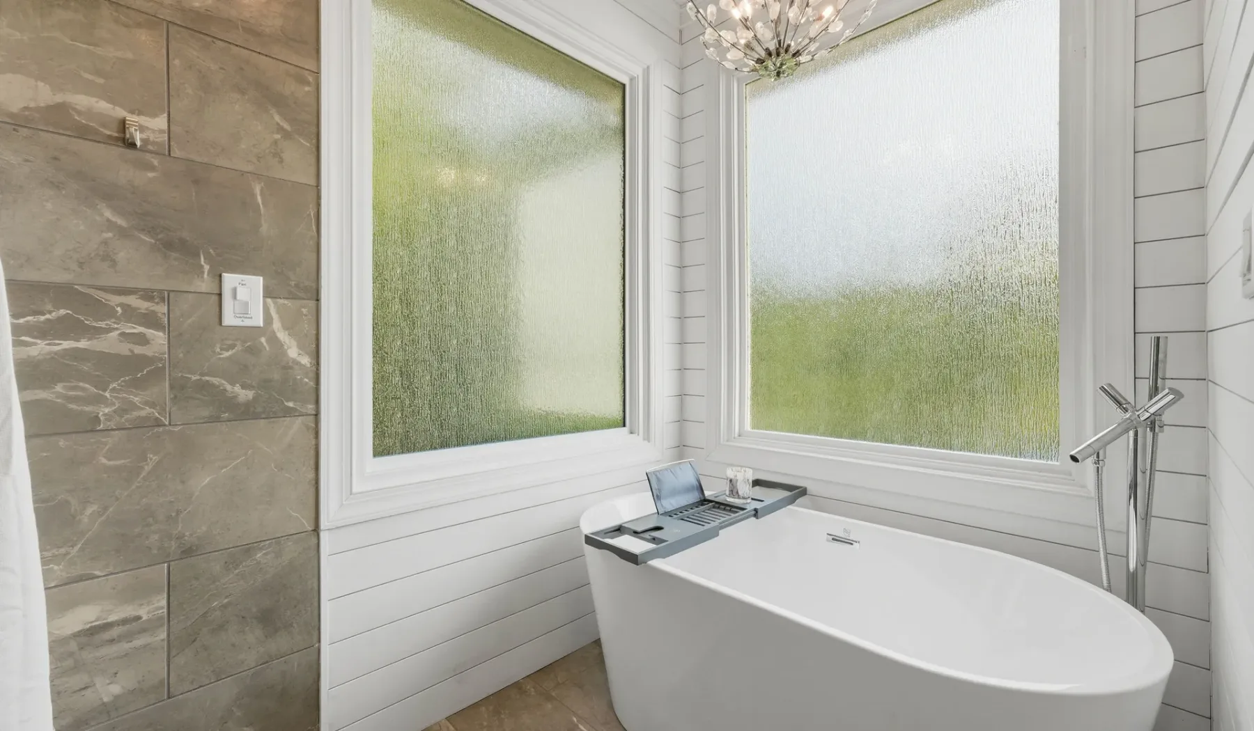 A bathroom with a freestanding bathtub beside large frosted windows.