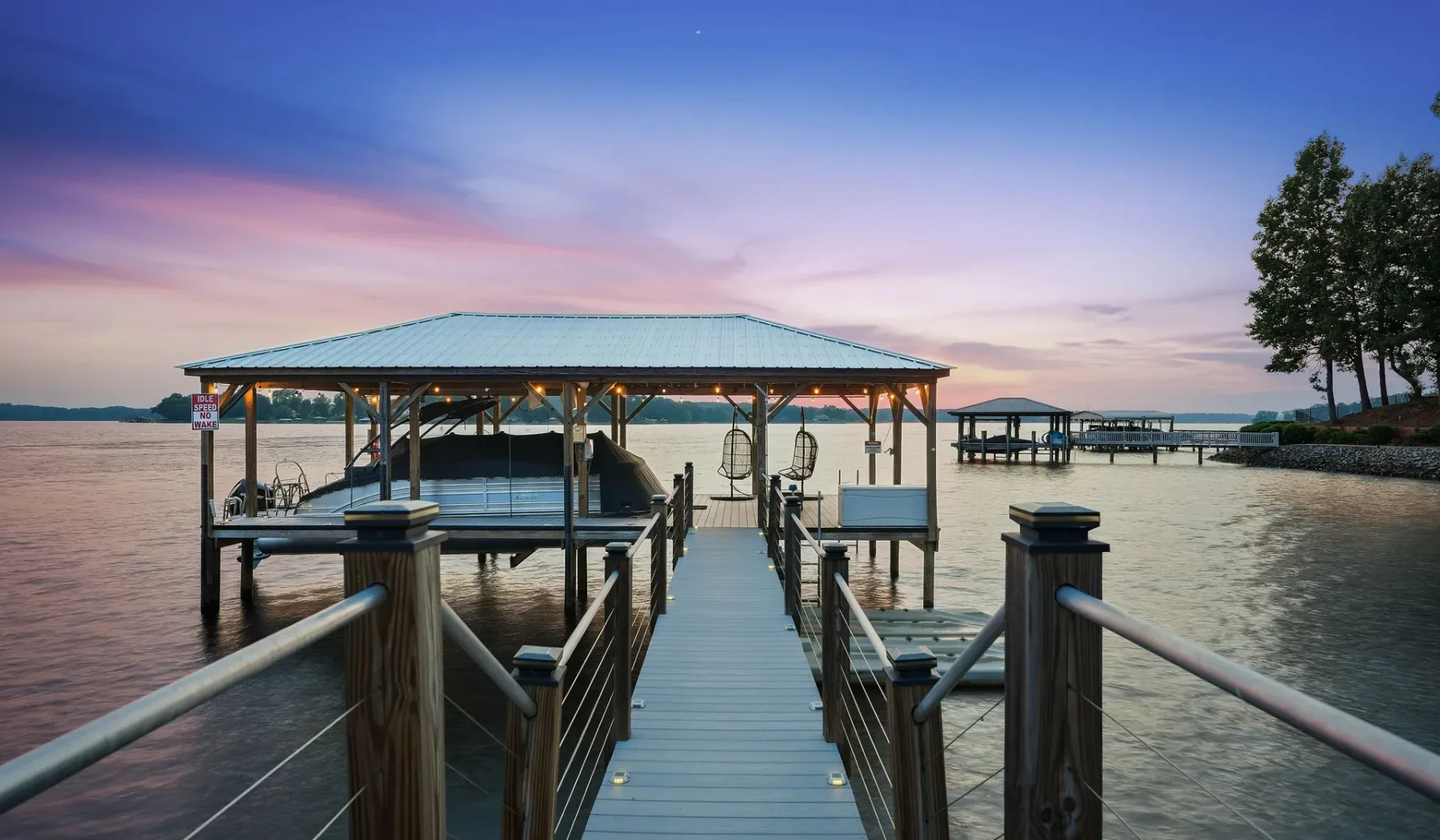 A covered dock extends over calm water beneath a colorful evening sky.