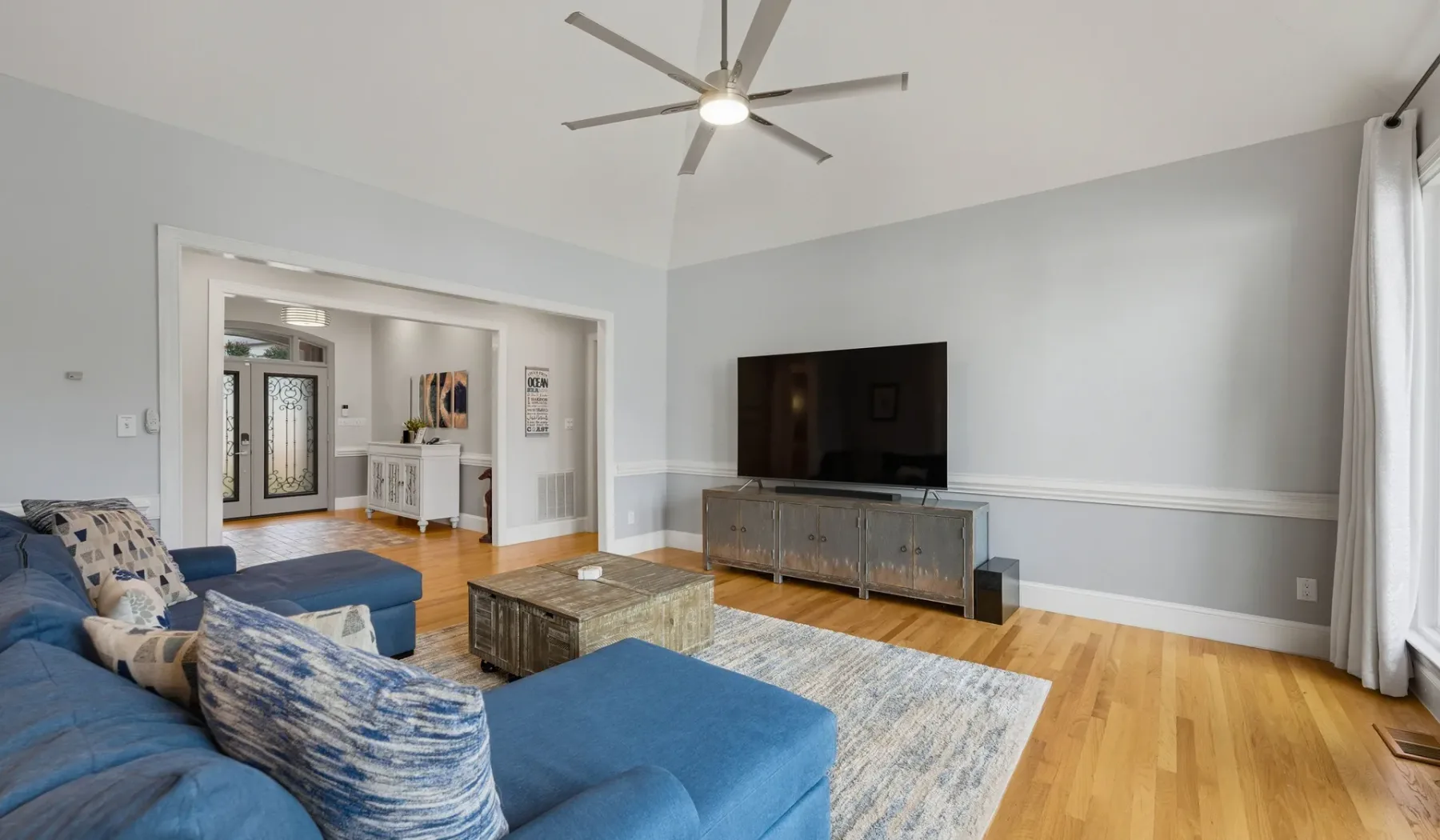 A living room with blue seating, a television, and a rug on a wood floor.
