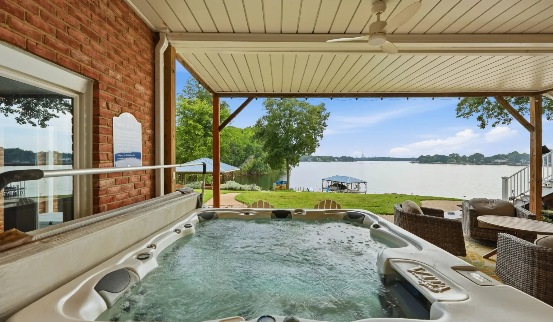A covered lakeside patio features a bubbling hot tub and outdoor seating.