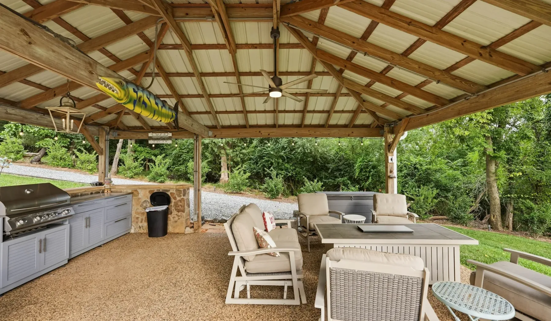 A covered outdoor dining and seating area with a grill and ceiling fan.