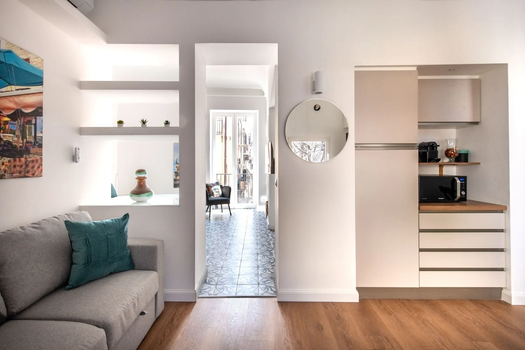 Una sala luminosa da a un pasillo con suelo de baldosas junto a una cocina compacta.