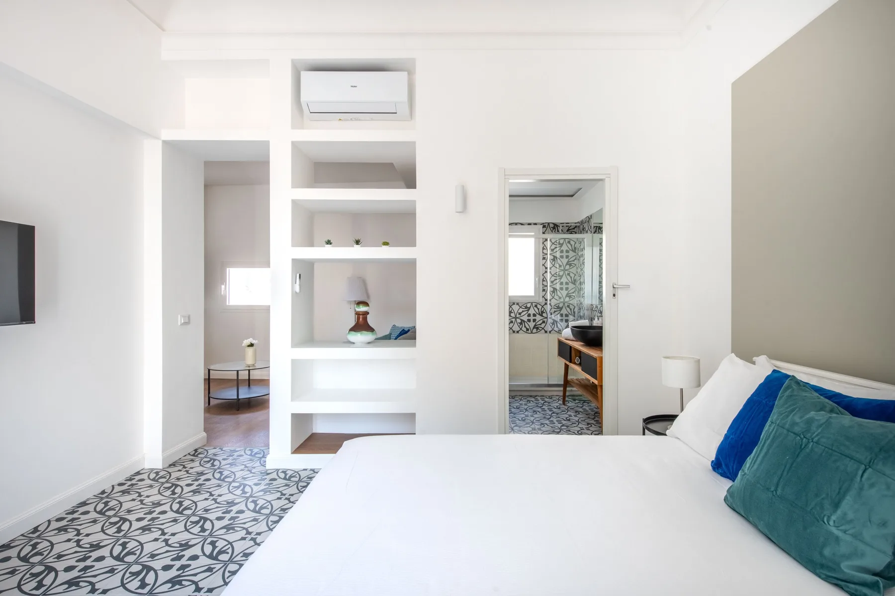 Un dormitorio luminoso con una cama blanca y un suelo de baldosas estampadas.