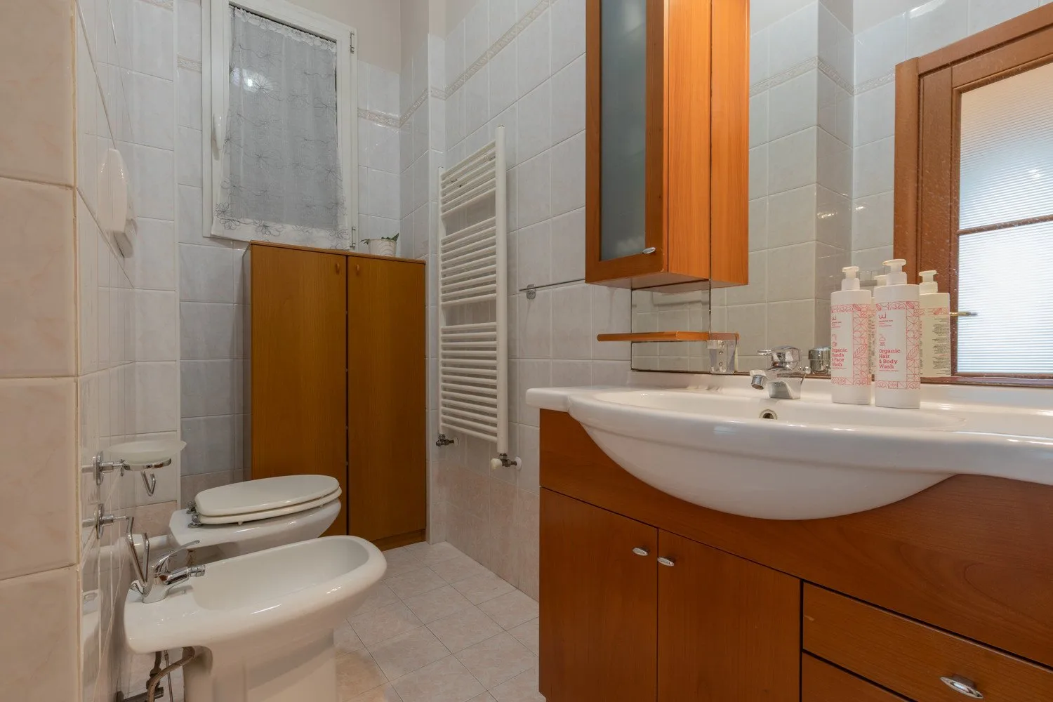 A tiled bathroom with a sink, toilet, bidet, and wooden vanity.