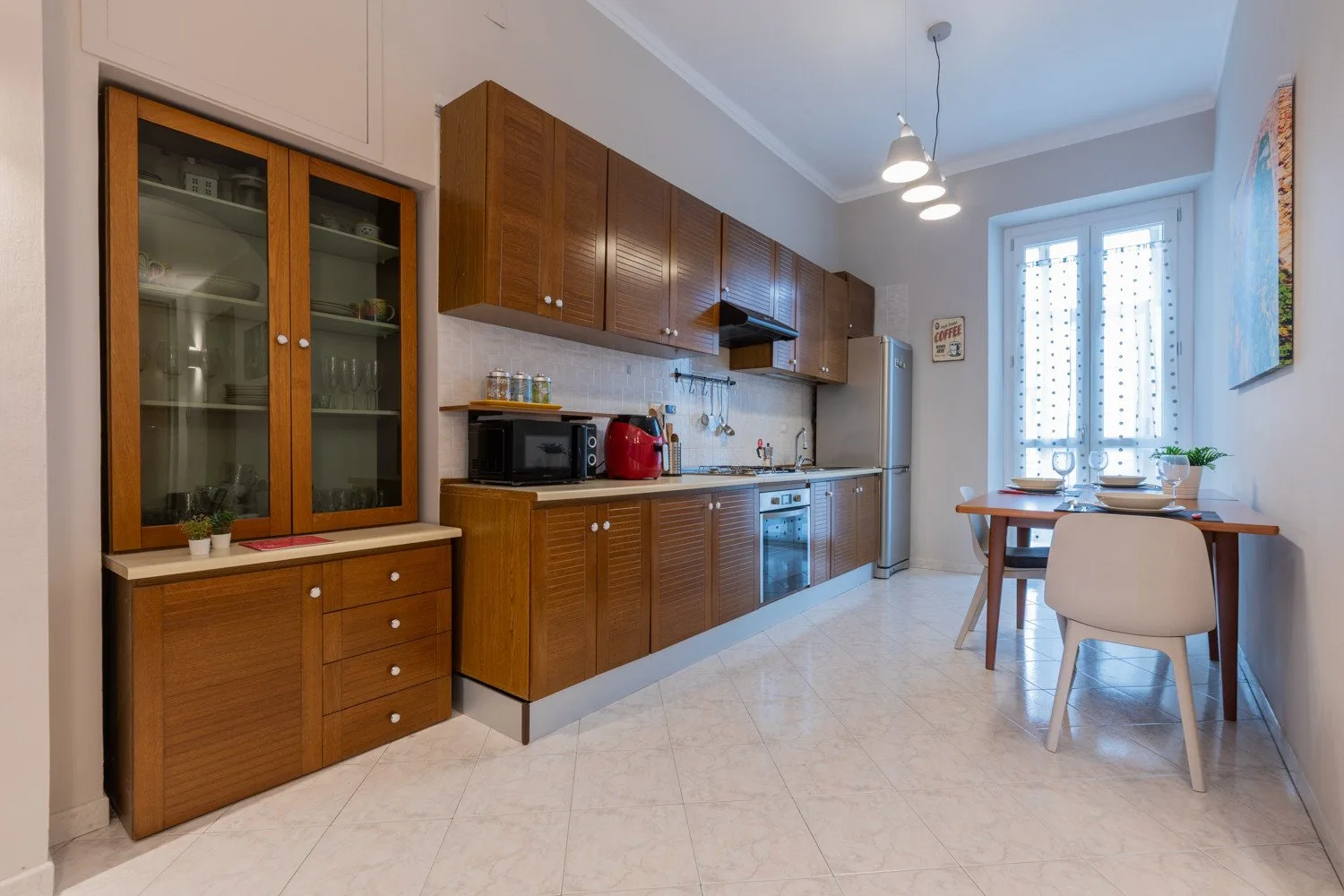 A kitchen with wooden cabinets, appliances, and a small dining table by the window.