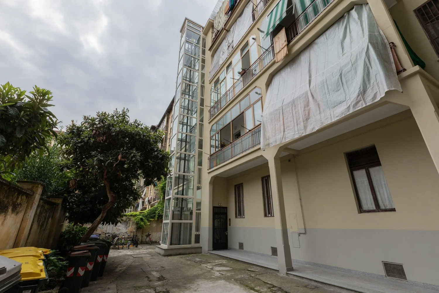 A multi-story building with a glass elevator shaft beside a paved courtyard.