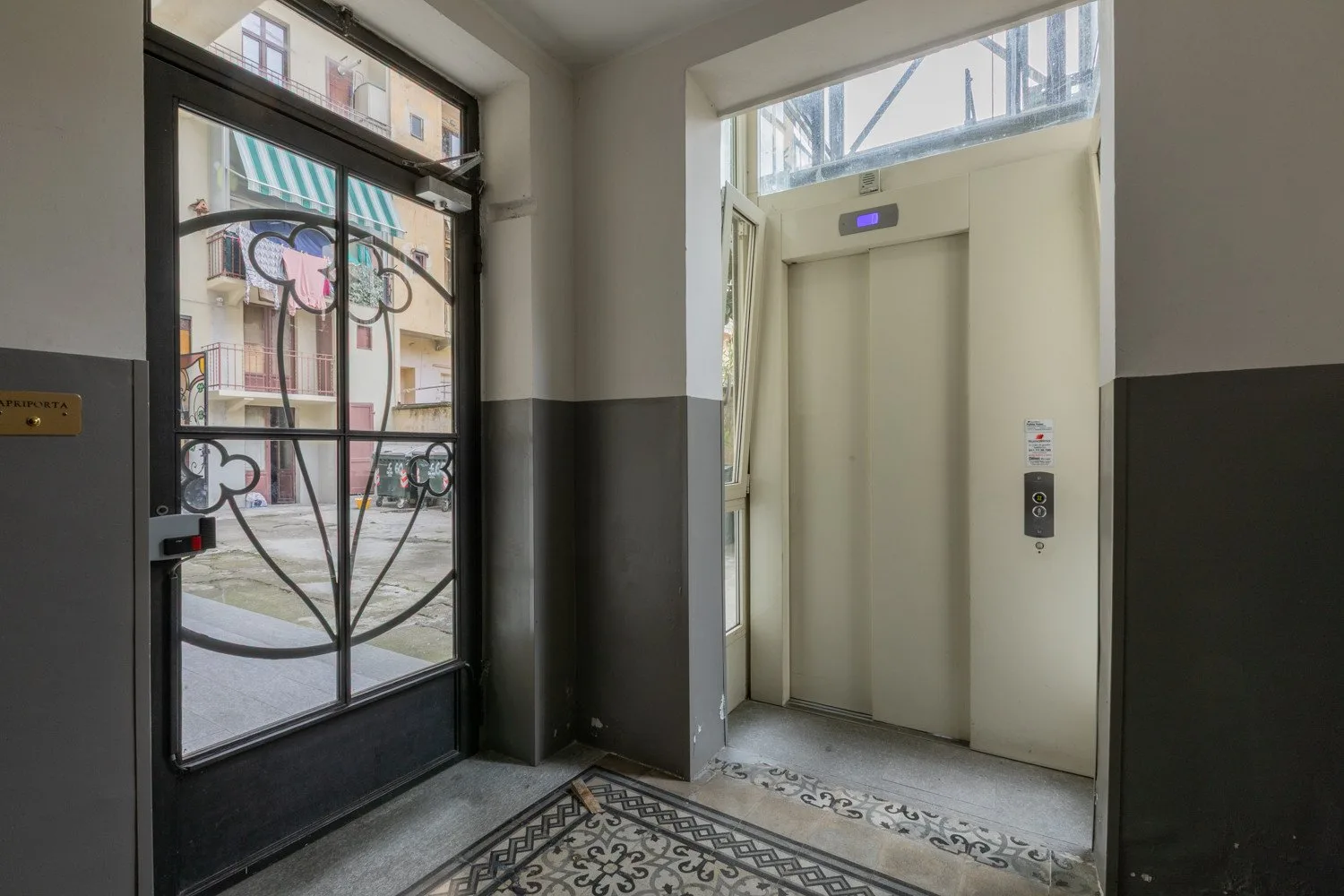 An elevator entrance beside a glass entry door, with a patterned floor mat.