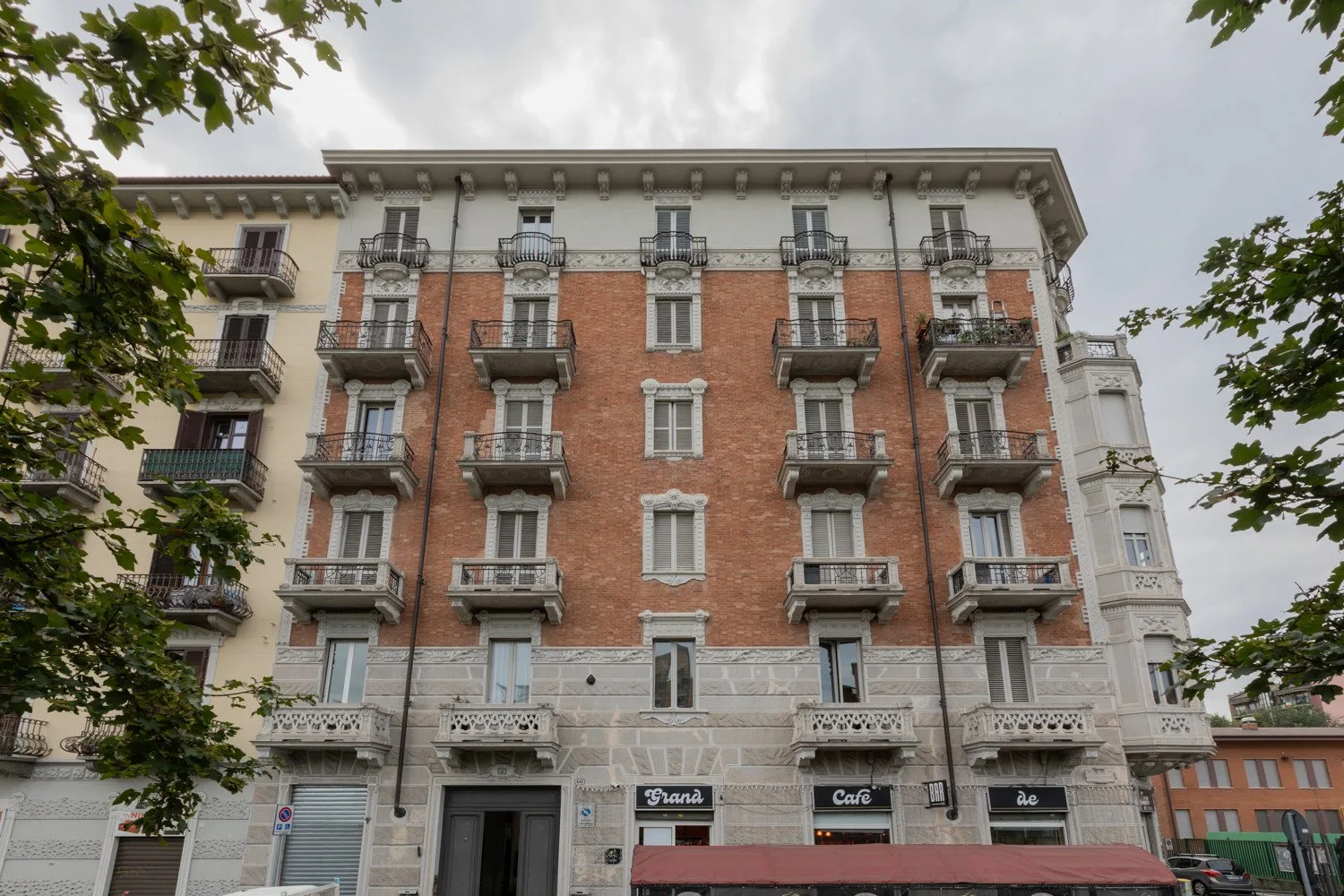 A brick city building with rows of balconies and ground-floor storefronts.