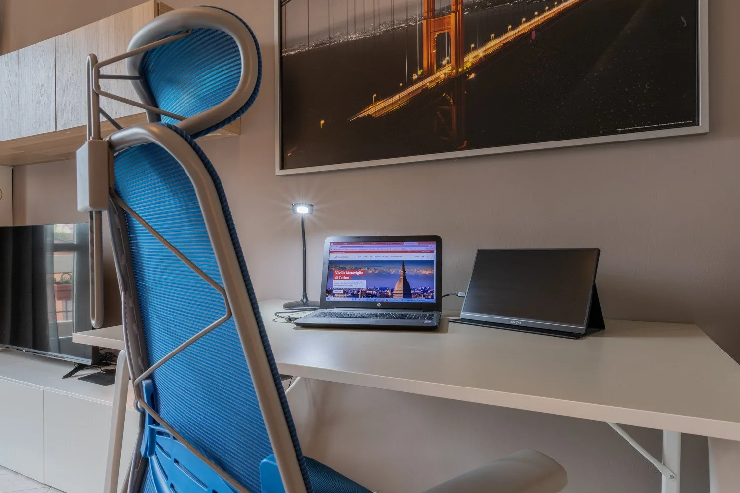 A modern workspace with a blue chair, desk, and computer screens.