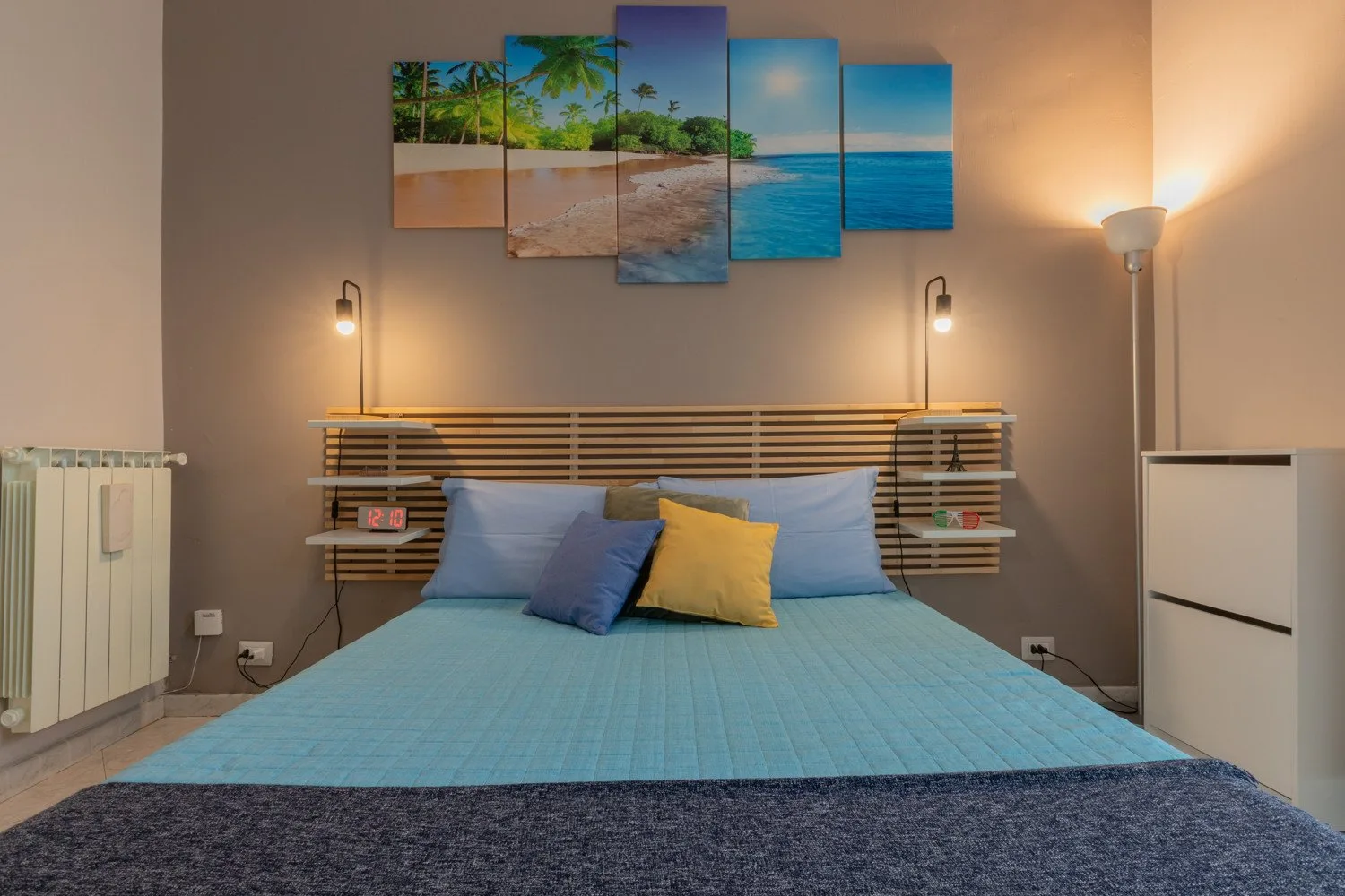 A bedroom with a bed dressed in blue bedding and beach artwork above the headboard.