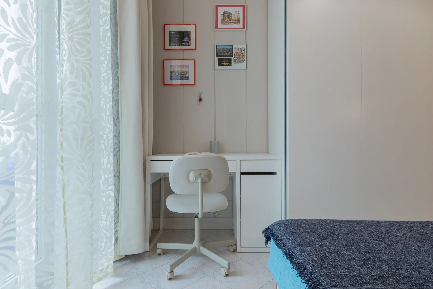 A small desk and chair sit beside a curtained window in a bright room.
