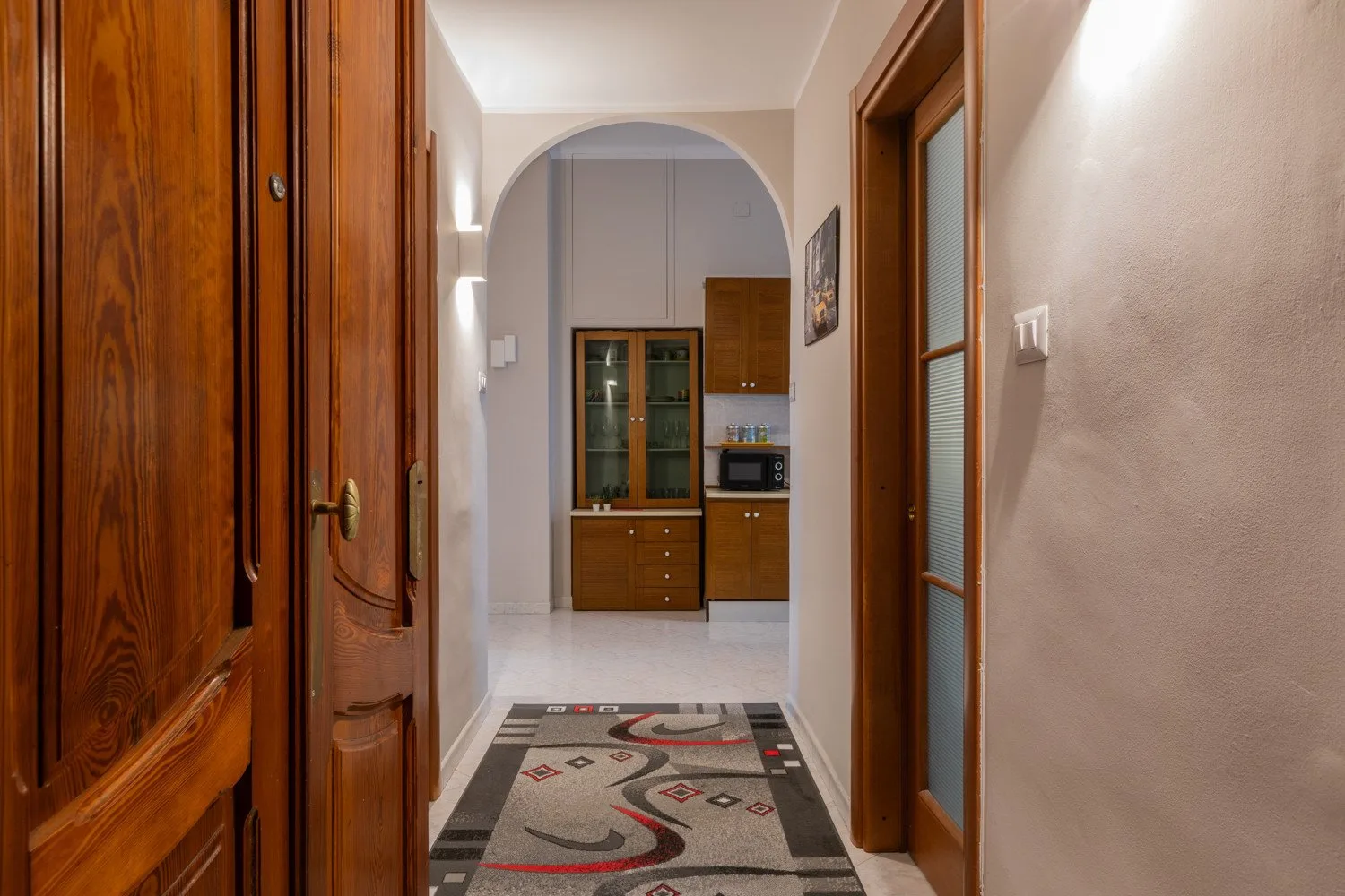 A hallway opens through an archway to a kitchen, with a patterned runner on the floor.