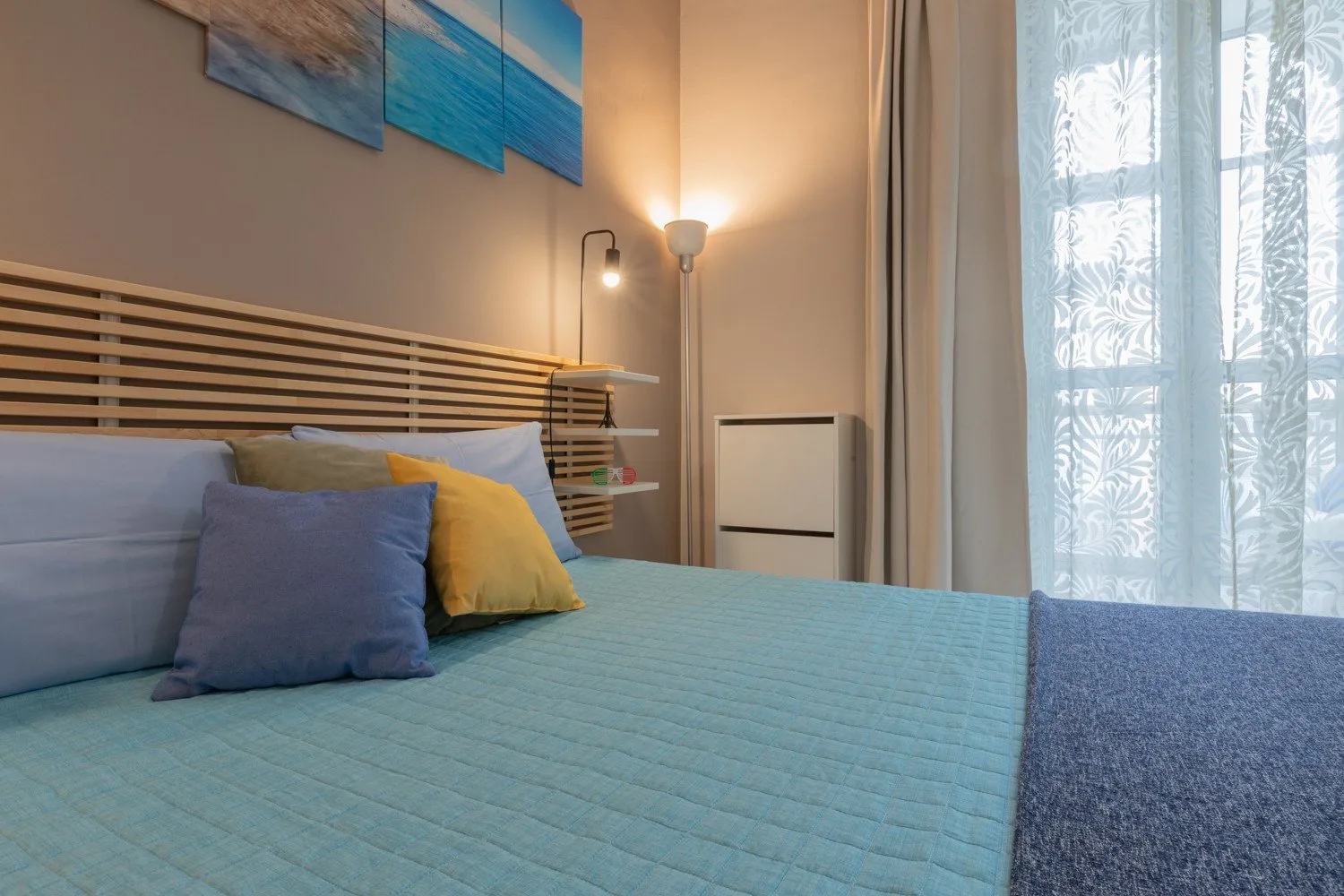 A bedroom with a bed dressed in blue bedding beside a curtained window.