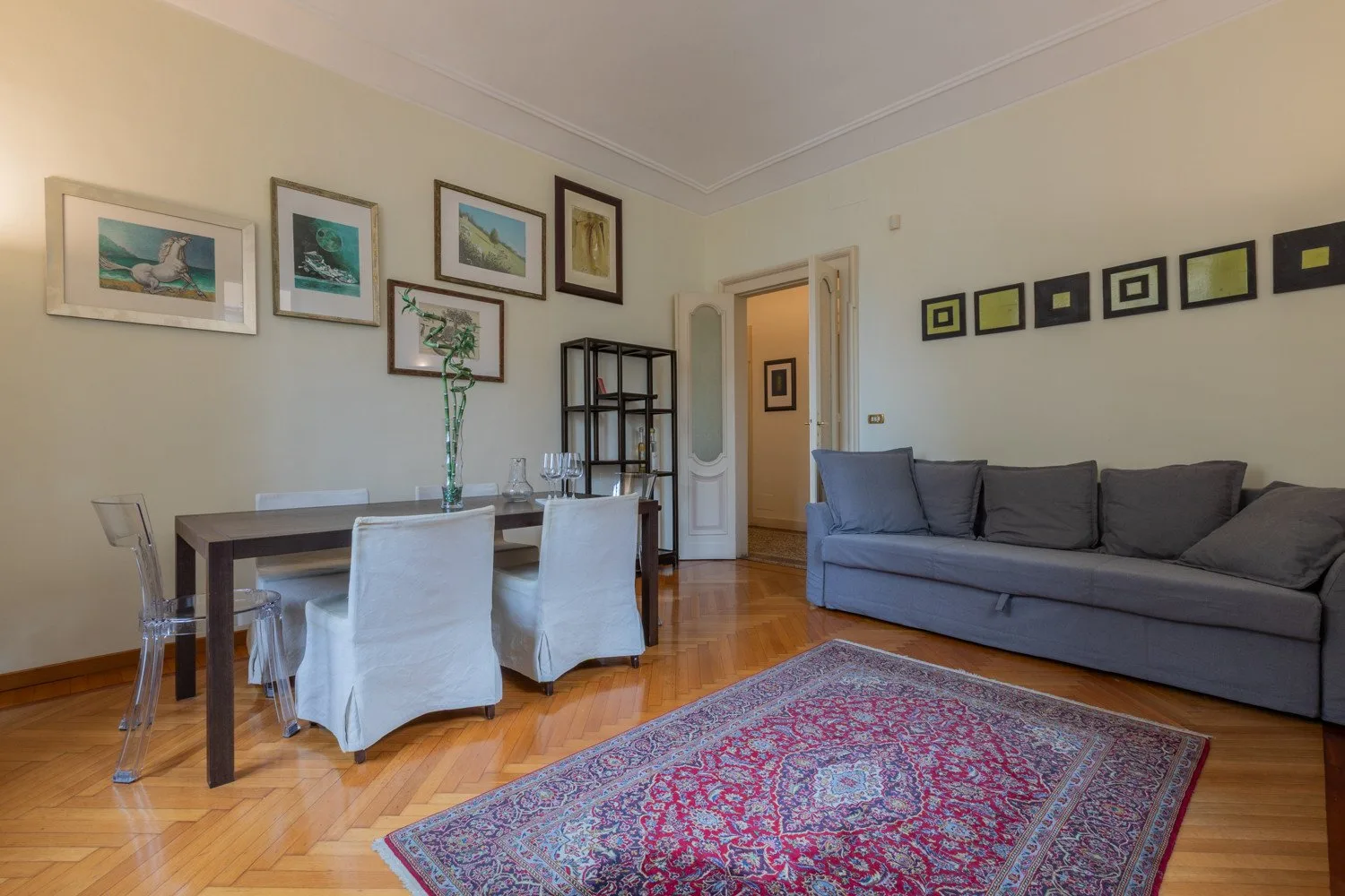 Sala de estar y comedor con asientos grises, una mesa de comedor y una alfombra estampada.