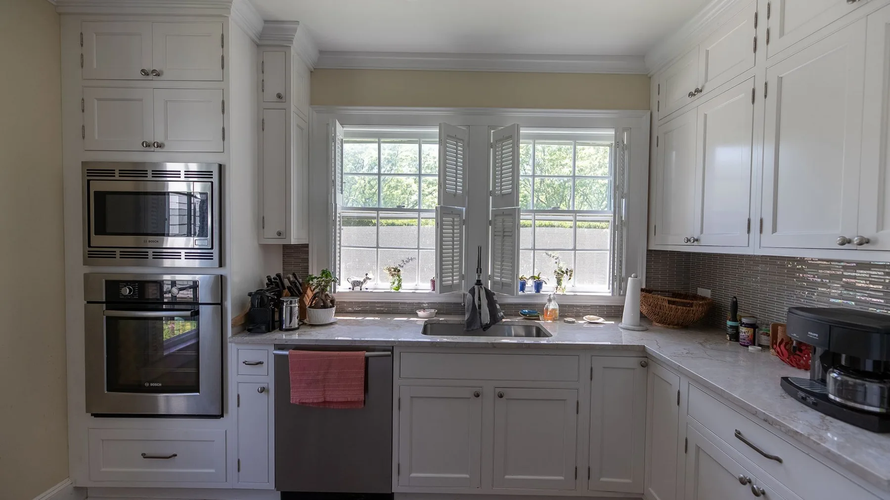 Una cocina luminosa con gabinetes blancos, un fregadero central y dos ventanas.