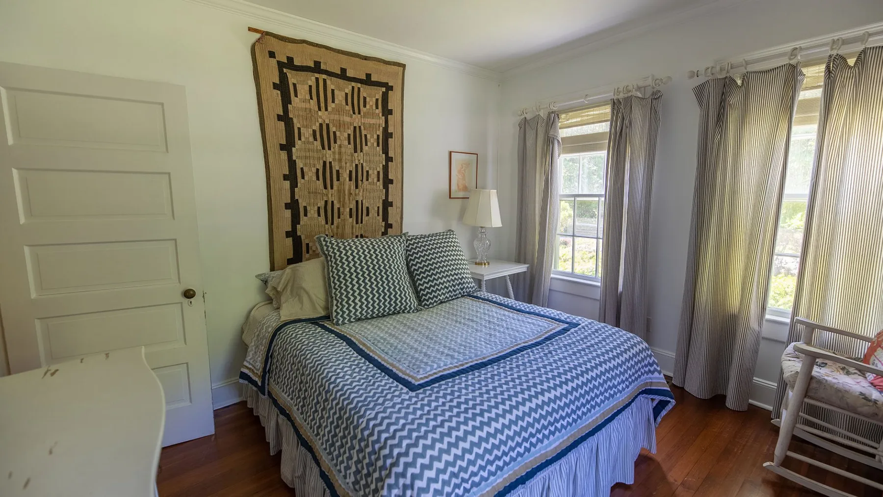 Un dormitorio con una cama bien tendida y ventanas altas con cortinas.