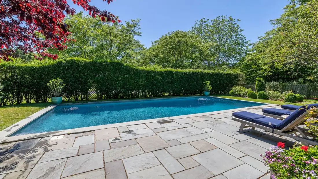 Una piscina al aire libre junto a un patio pavimentado y asientos de descanso.