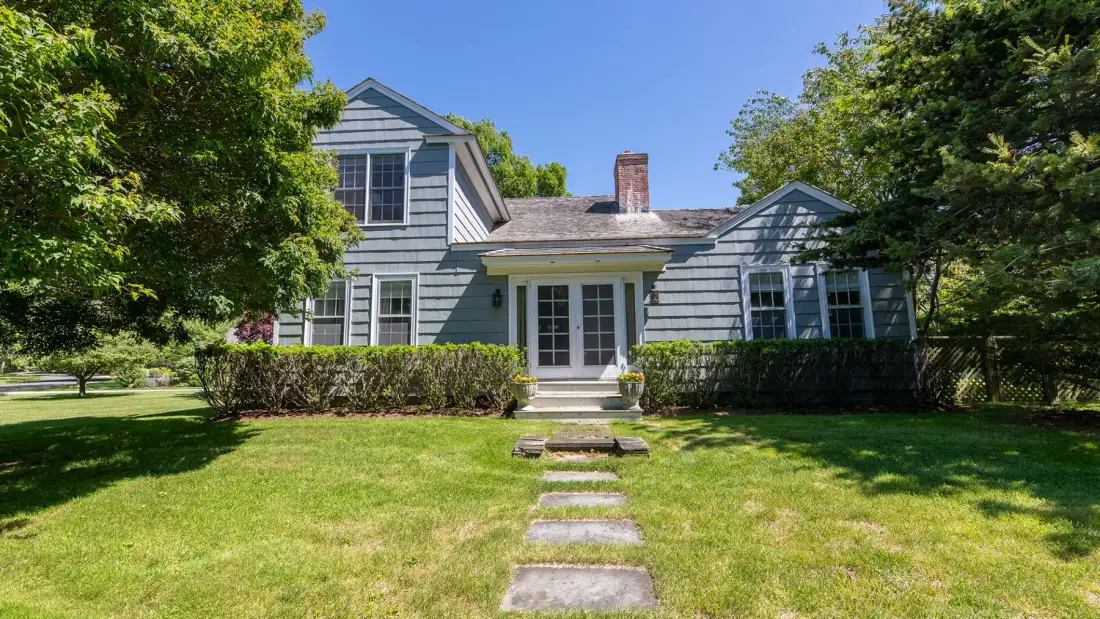 Una casa gris se encuentra detrás de un césped verde y piedras de paso.