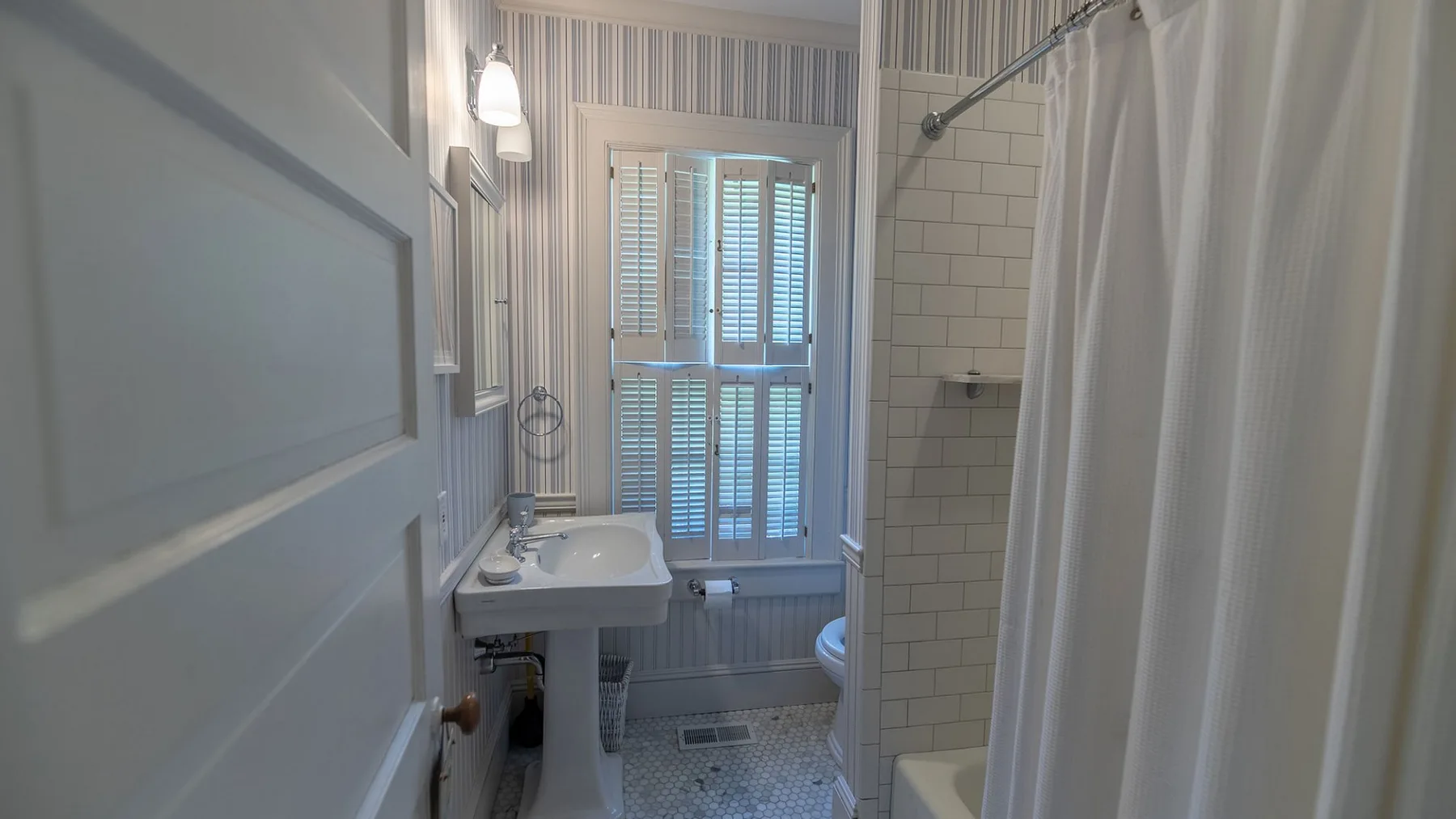 Un baño con lavabo, ducha de azulejos y ventana con contraventanas.