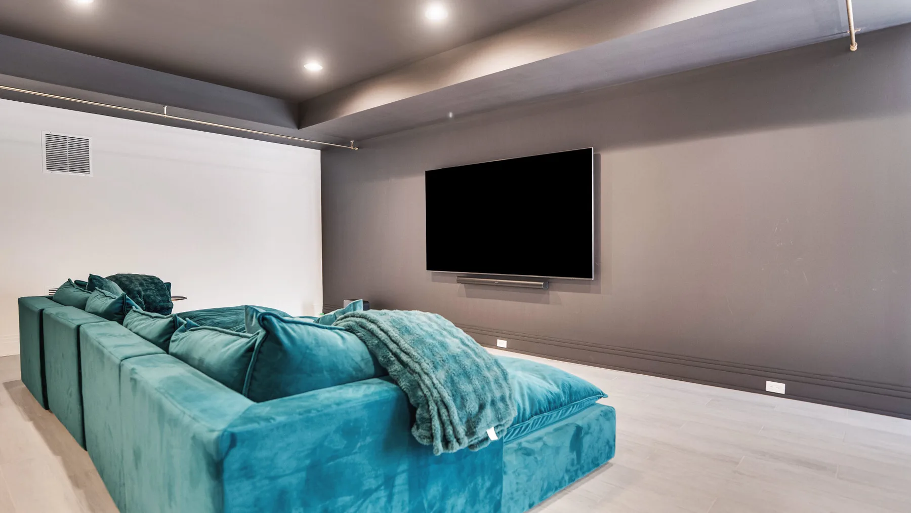 Una sala de estar con asientos turquesa frente a un televisor montado en la pared.