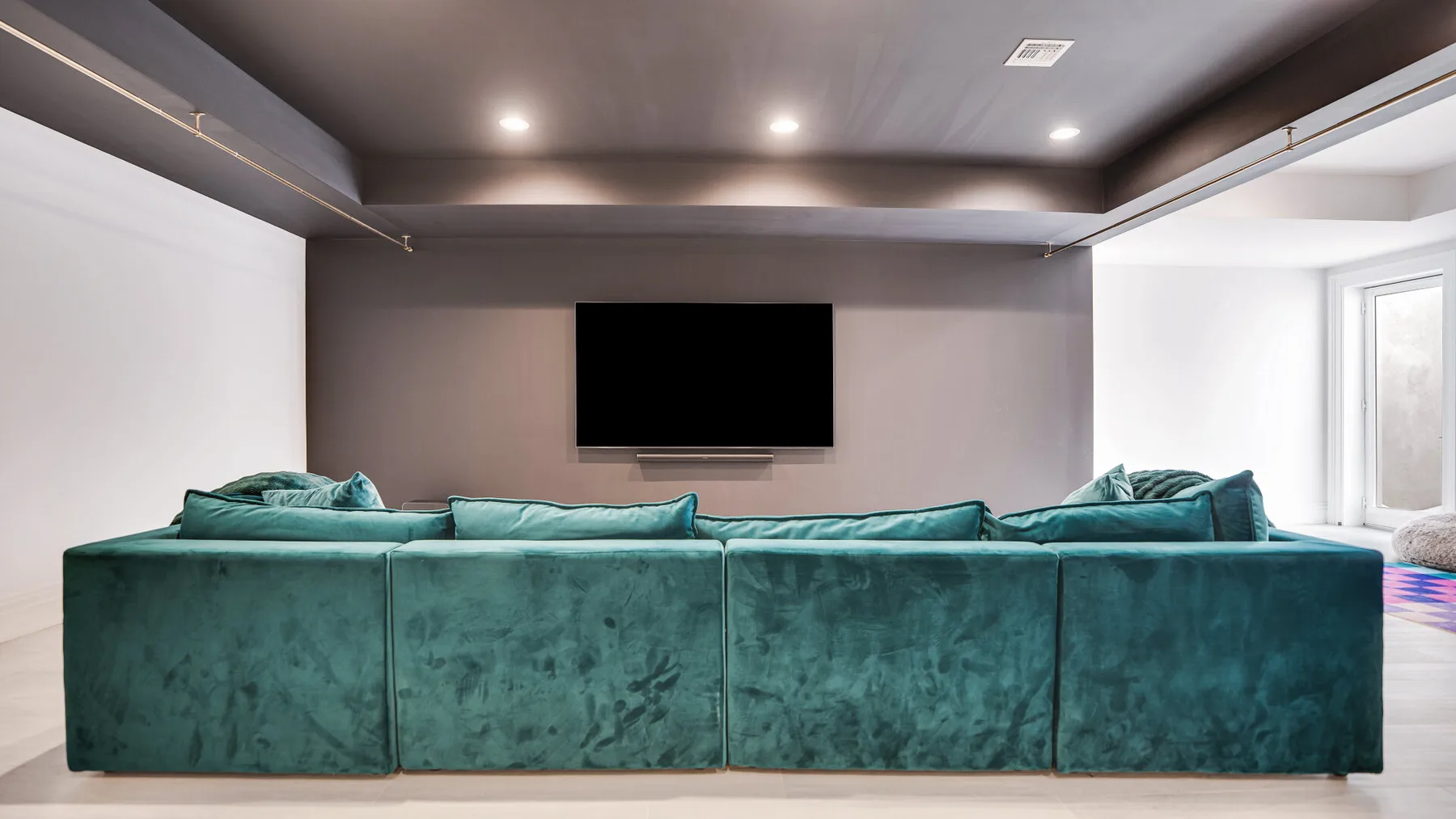 Una sala de estar con asientos color turquesa frente a un televisor montado en la pared.